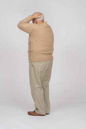一位身穿休闲服的老人手放在头上站立的侧视图