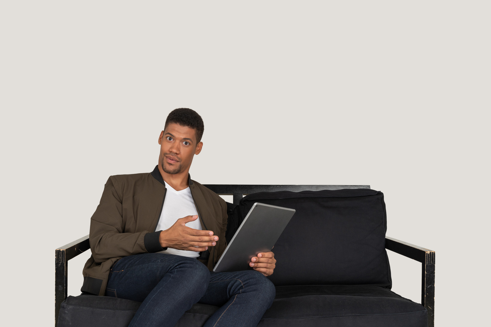 Front view of a shocked young man sitting on a sofa while watching the tablet