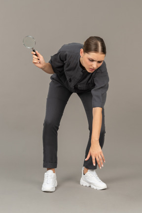 Front view of a young woman in a jumpsuit holding a magnifying glass