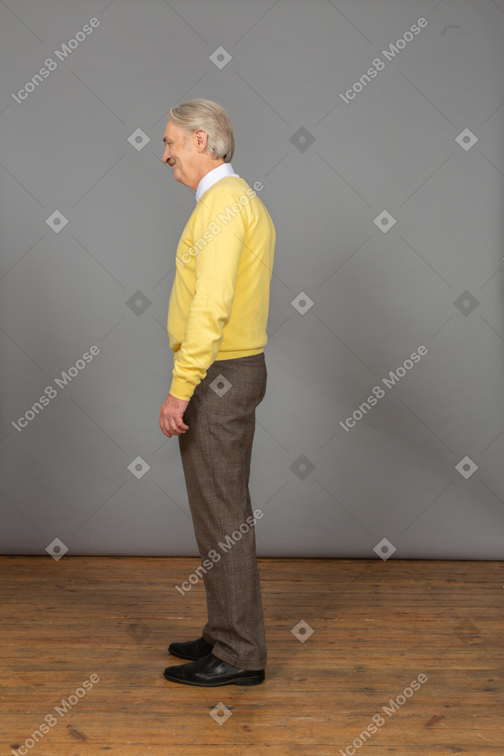 惊讶的老人，在黄色的套衫弯下腰，放在一边看的侧视图