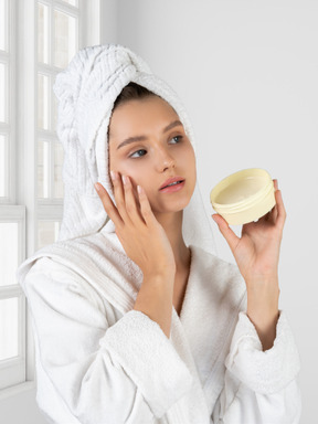 A woman in a bathrobe is holding a jar of cream
