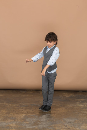 Vista frontal de un niño en traje de pie con los brazos extendidos