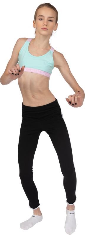 Vista frontal de uma adolescente em roupas esportivas, levantando as mãos e a perna enquanto dançava
