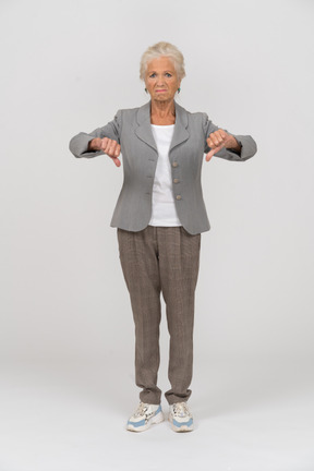 Vista frontal de uma senhora idosa de terno mostrando os polegares para baixo