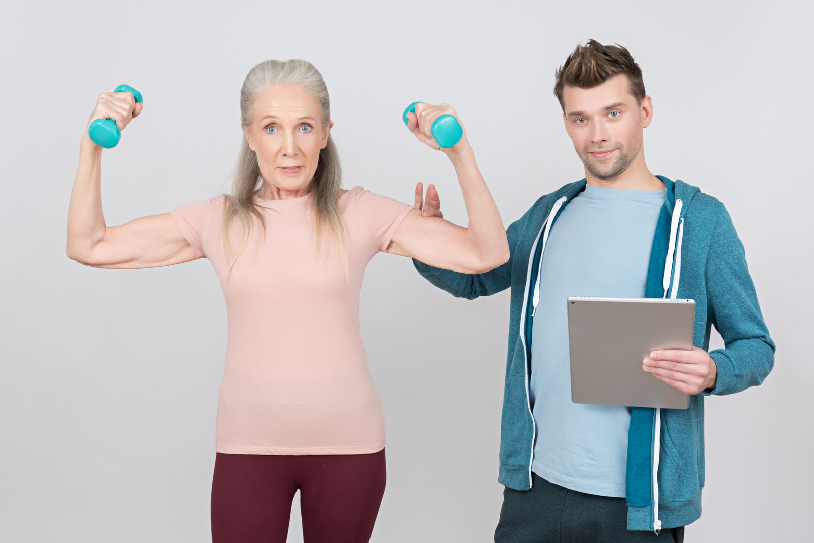 Young guy holding tablet and old woman lifting hand weights and showing her muscles