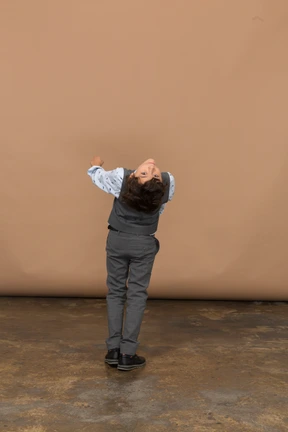 Rear view of a boy in grey suit bending and looking at camera