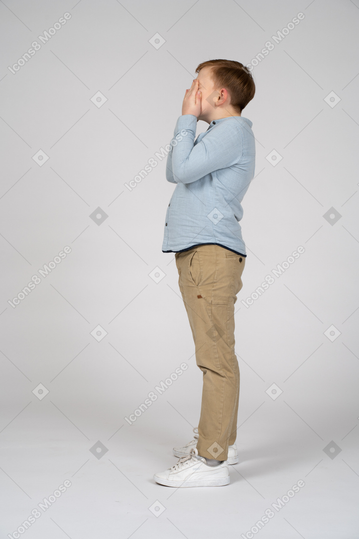 Side view of a boy covering face with hands