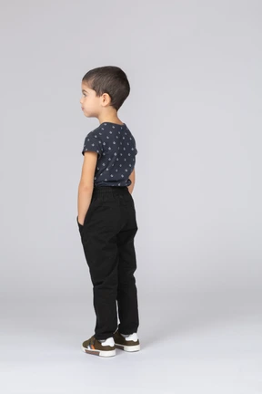 Side view of a cute boy in casual clothes posing with hands in pockets