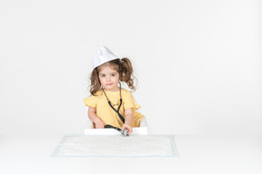 Bambina vestita come un dottore seduto al tavolo