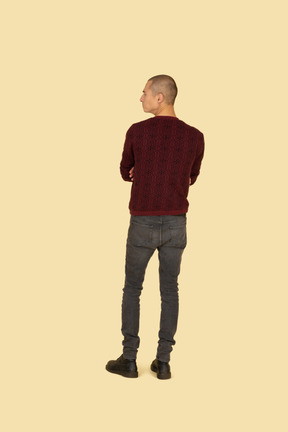 Back view of an offended young man dressed in casual clothes crossing his hands