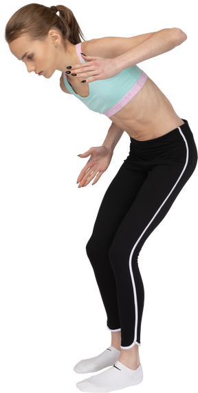 Vista lateral de una jovencita en ropa deportiva inclinada hacia adelante mientras está de pie como un robot