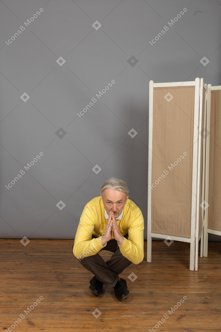 Front view of a squatting old man showing a namaste sign