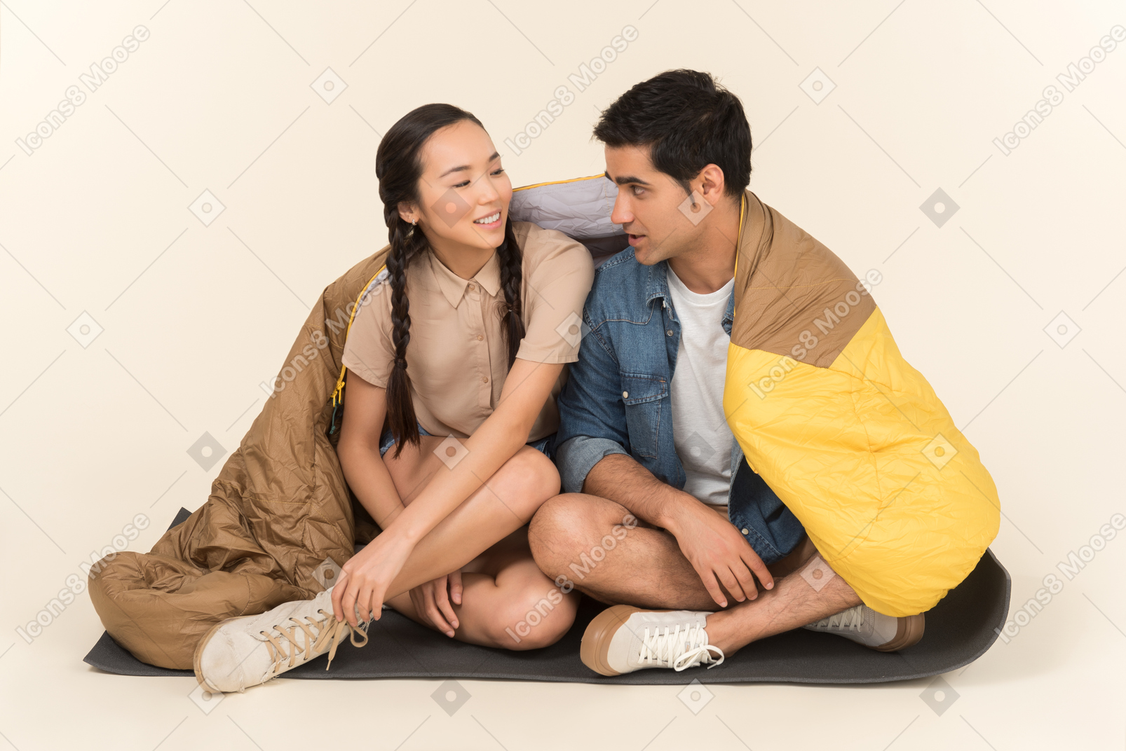 Young woman wrapped in sleeping bag and man sitting on karimat