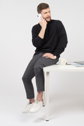 Frown office worker sitting on white desk and talking on the phone