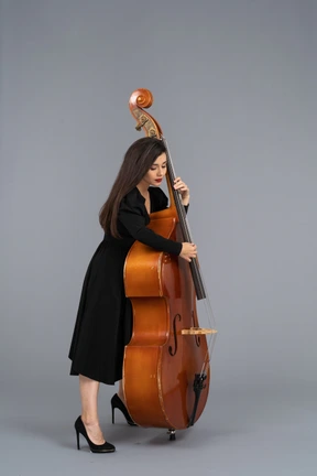 Vista lateral de un joven músico serio en vestido negro tocando su contrabajo