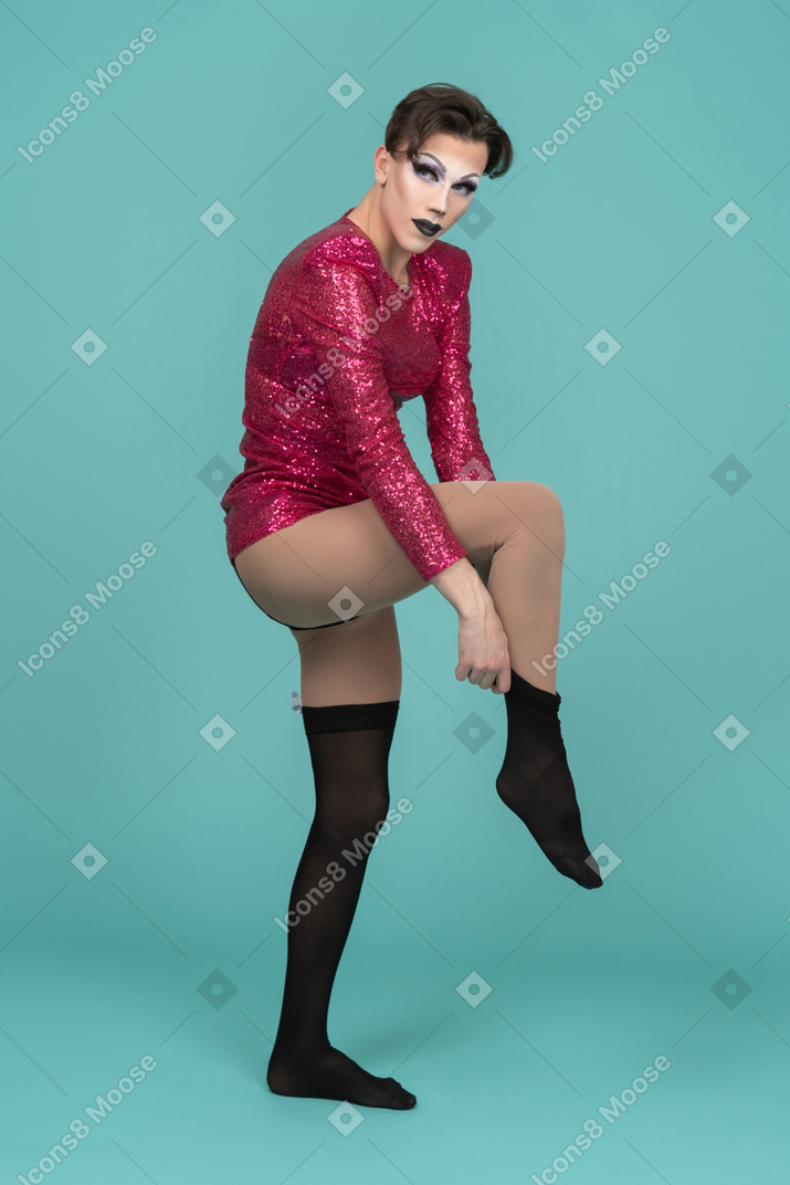 Drag queen in pink dress putting on black stocking