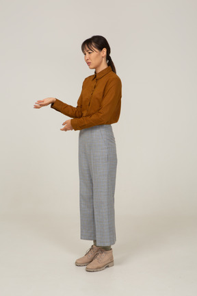 Vista di tre quarti di una giovane donna asiatica premurosa e gesticolante in calzoni e camicetta