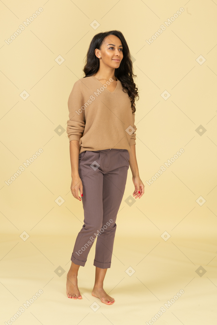 Вид в три четверти темнокожей молодой женщины, стоящей неподвижно и улыбаясь