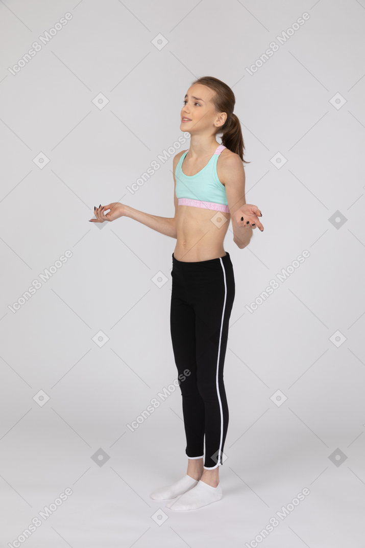 Вид в три четверти девушки-подростка в спортивной одежде, поднимающей руки и рассуждающей