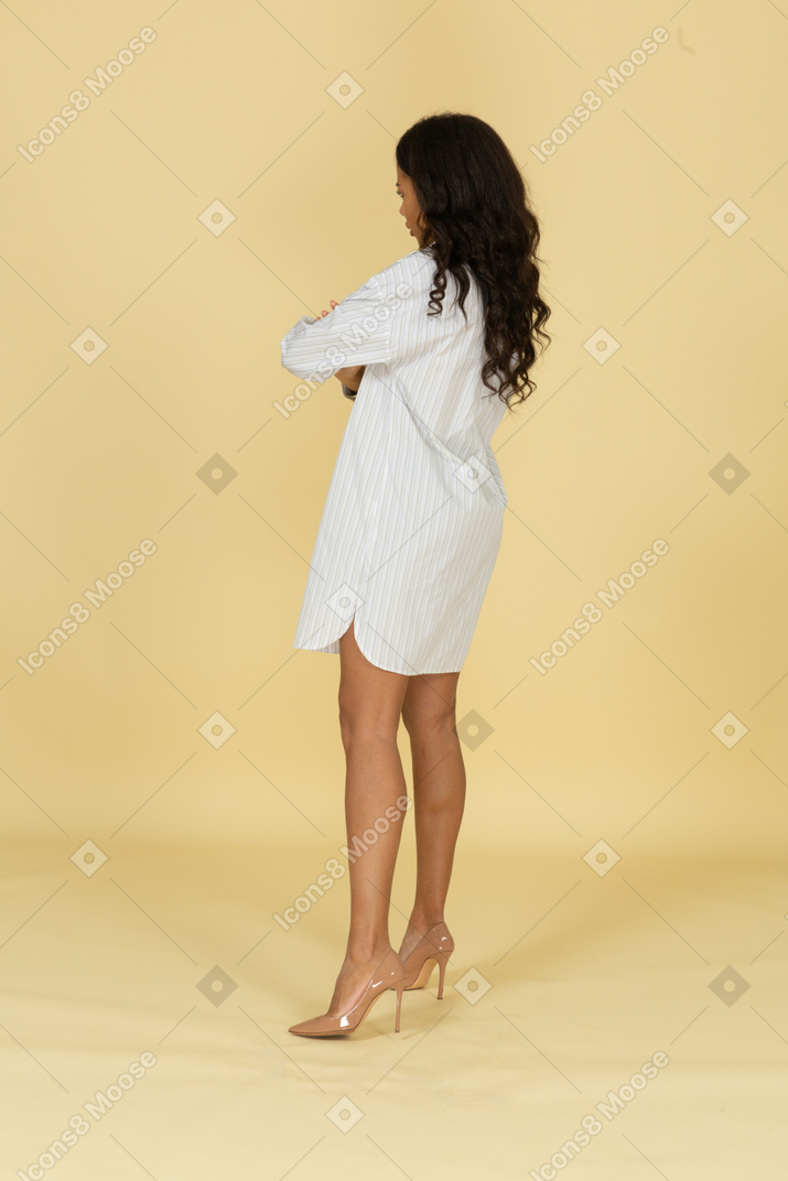 Side view of an offended dark-skinned young female in white dress crossing hands