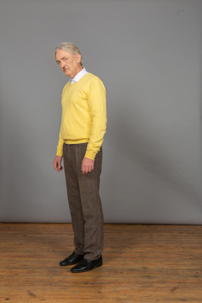 Vista de três quartos de um homem velho e triste em um pulôver amarelo, inclinado para a frente e olhando para a câmera