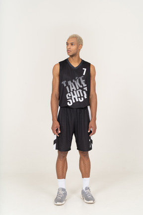 一个年轻的男篮球运动员站着不动，看着一边的前视图