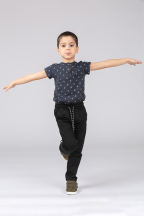 Вид спереди симпатичного мальчика, балансирующего на одной ноге и вытягивающего руки