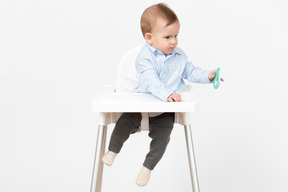 Baby boy sentado en una silla alta y sosteniendo juguetes