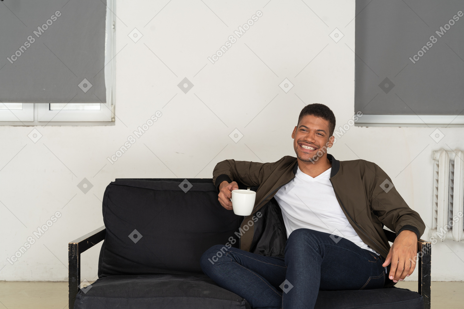 Front view of a smiling young man sitting on a sofa with a cup of coffee