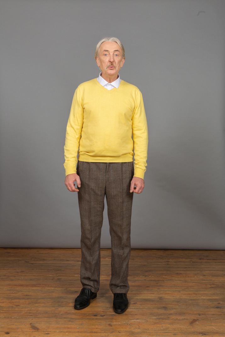 Front view of an old pouting man in yellow pullover leaning forward and grimacing while looking at camera