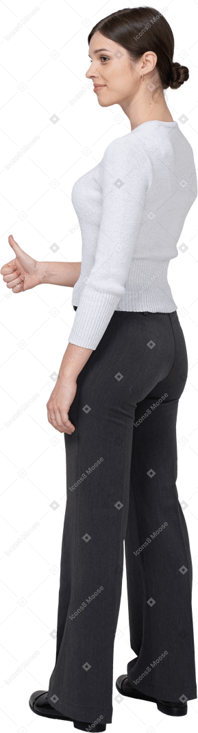 Вид сзади на три четверти жизнерадостной молодой женщины в офисной одежде, показывающей большой палец вверх