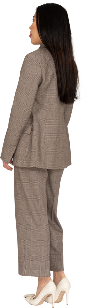 Three-quarter back view of a young lady in brown business suit showing tongue
