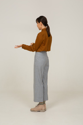 Vista posterior de tres cuartos de una joven mujer asiática cuestionando en calzones y blusa levantando las manos