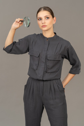 Front view of young woman in a jumpsuit holding a magnifying glass