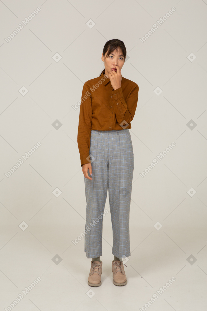 一位身着马裤和衬衫的年轻亚洲女性抚摸嘴巴的前视图