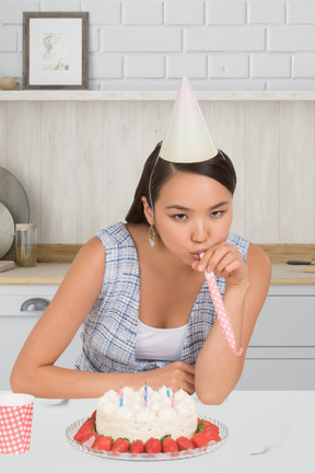 Woman in party hat blowing a party horn near birthday cake