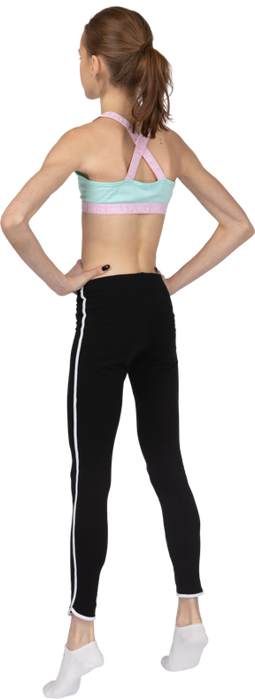 Dreiviertel-rückansicht eines jugendlichen mädchens in sportbekleidung, das hände auf hüften setzt, während es auf zehenspitzen steht