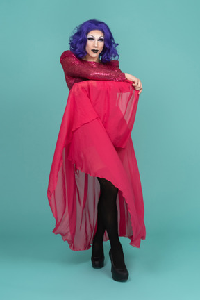 Drag queen in pink dress holding up long skirt while posing