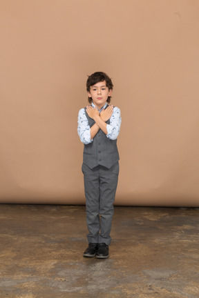 Vue de face d'un garçon mignon en costume debout avec les mains sur les épaules