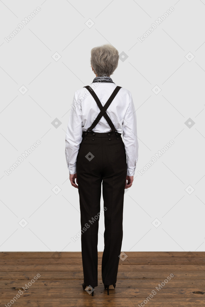 Vista traseira de uma mulher idosa com suspensórios parada em uma sala vazia