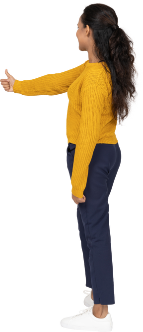 Vista lateral de una niña feliz en ropa casual mostrando el pulgar hacia arriba