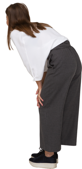 Vista posteriore di tre quarti di una giovane donna in abiti da ufficio che si piega e tocca il ginocchio