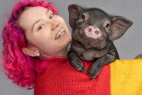 Pinkhaarige frau, die ein kleines ferkel hält