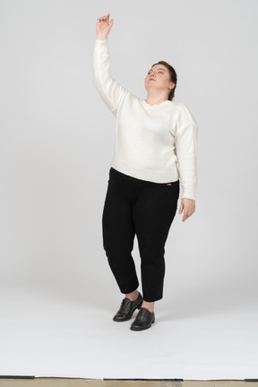 Вид спереди впечатленной женщины больших размеров в повседневной одежде, указывающей вверх рукой