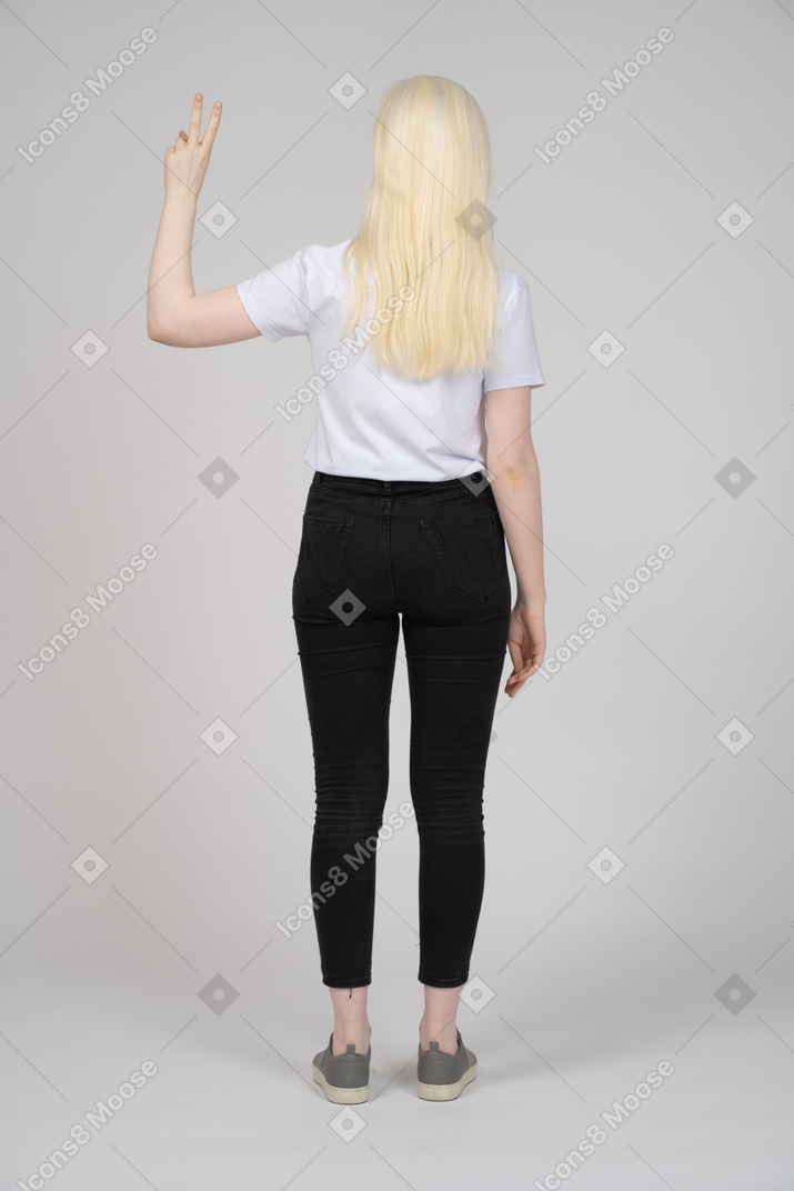Vista posteriore di una giovane ragazza in piedi con il segno della mano di pace