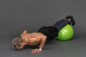 Vue de trois quarts d'un homme afro torse nu faisant des pompes sur un ballon de gymnastique