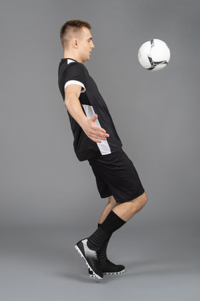 Side view of a male football player and a flying ball