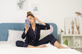 Vue de face d'une jeune femme en pyjama prenant selfie au lit