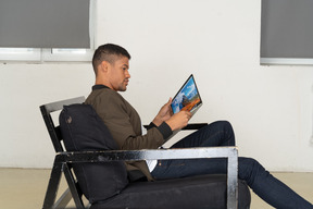 Side view of young man sitting on a sofa and holding a laptop