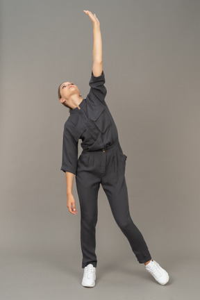 Front view of a young woman in a jumpsuit raising hand